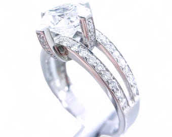 May include: A silver engagement ring with a large, clear, round diamond in the center. The band is set with smaller diamonds that continue down the sides of the ring.