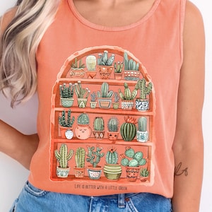 May include: A terracotta sleeveless tank top with a graphic of a shelf full of potted cacti and succulents. The text "Life is better with a little green" is printed below the graphic.