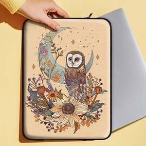 May include: A beige laptop sleeve featuring a whimsical illustration of an owl perched on a crescent moon surrounded by flowers and stars. The owl has brown and white feathers and large, round eyes.