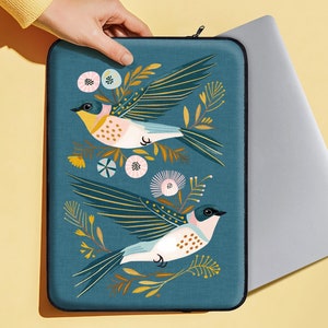 May include: A teal blue laptop sleeve with a floral design featuring two stylized birds with yellow, pink, and white accents. The birds are flying in opposite directions.