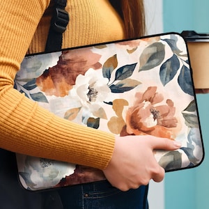 May include: A woman is holding a floral laptop sleeve with a black background and a white, brown, and blue floral pattern. She is also holding a brown takeaway cup.