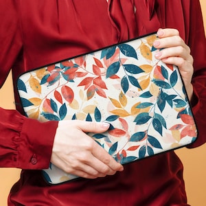 May include: A laptop sleeve with a colorful floral pattern featuring leaves and branches in shades of red, yellow, blue, and green on a white background.