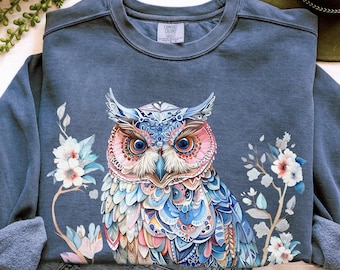 Pode incluir: Uma camisola azul com uma coruja colorida e um design floral. A camisola é tingida em peça para um look vintage e tem um fleece macio, tecido de peso médio e um caimento relaxado.
