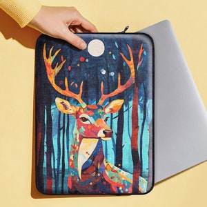 Könnte beinhalten: Eine farbenfrohe Laptoptasche mit einem stilisierten Hirsch mit großen Geweih in einer Waldlandschaft. Der Hirsch ist in Rot-, Orange-, Gelb-, Blau- und Grüntönen auf einem dunkelblauen Hintergrund gemalt.