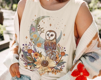 Op de afbeelding: Ivoor tanktop met een gedetailleerde illustratie van een uil op een maan, omringd door bloemen en sterren. Een grote zonnebloem staat onderaan het ontwerp. Het woord "IVORY" staat rechtsonder gedrukt.