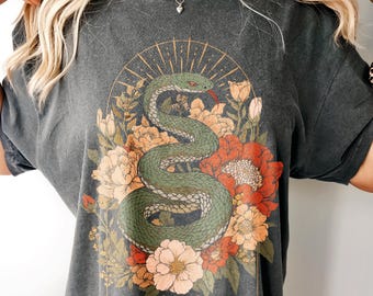 Könnte beinhalten: Ein anthrazitfarbenes T-Shirt mit einem Grafikdruck einer grünen Schlange, die sich zwischen orangefarbenen, roten und cremefarbenen Blumen windet. Das Design zeigt einen Sonnenstrahlenbogen und Mondphasen. Das Wort Pepper ist abgebildet.