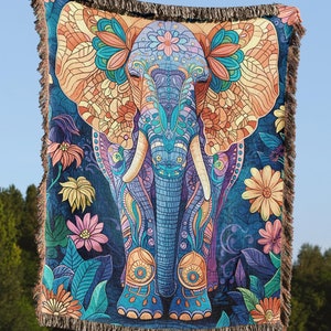 May include: A woven tapestry featuring a colorful, detailed illustration of an elephant with floral patterns. The elephant is blue, purple, and orange, with intricate designs on its body and trunk. The background is a dark blue with green and yellow floral accents.