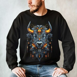 May include: A black sweatshirt with a graphic print of a blue bull's head with a third eye and ornate gold and orange accents.