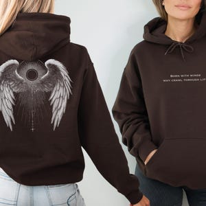 May include: Two brown hoodies. One features angel wings on the back, the other has the text "BORN WITH WINGS WHY CRAWL THROUGH LIFE?" in white. Both have a drawstring hood and a front pocket.