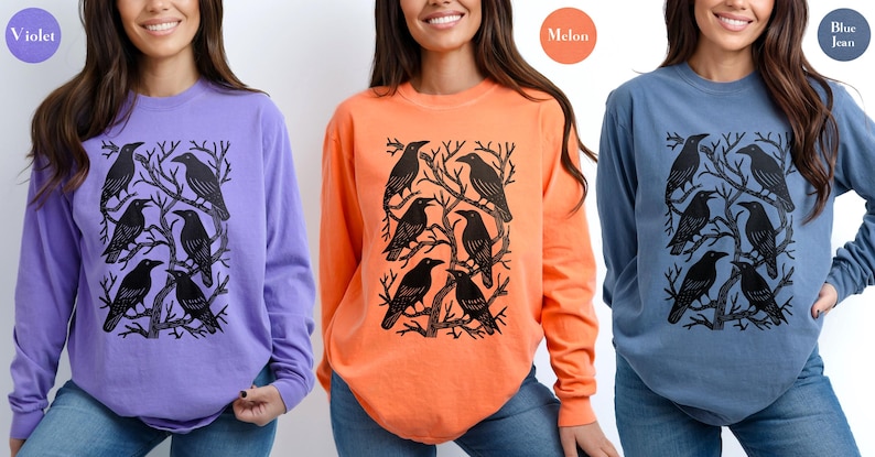May include: Long-sleeved shirts in violet, melon, and blue jean colors. Each shirt features a black graphic of crows perched on tree branches. The shirts are made of a soft material and are suitable for casual wear.