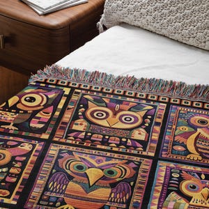May include: A woven throw blanket with a black background and a colorful geometric pattern of owls. The owls are in different colors, including yellow, orange, purple, and green. The blanket has a fringe border.