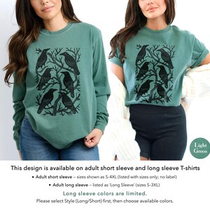 May include: Light green long-sleeve and short-sleeve t-shirts. Each shirt features a black graphic of crows perched on tree branches. The design is available in adult sizes S-4XL for short sleeves and S-3XL for long sleeves.