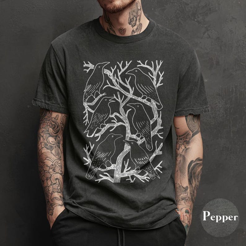 May include: Dark grey t-shirt featuring a white graphic of several crows perched on tree branches. The design is centered on the shirt, with the word "Pepper" visible in the lower right corner. The shirt has short sleeves and a crew neck.