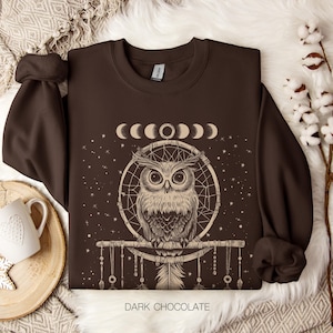 May include: A brown sweatshirt with a graphic of an owl in a dreamcatcher with a crescent moon design. The text "DARK CHOCOLATE" is printed on the bottom of the sweatshirt.
