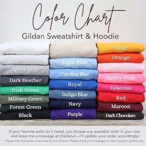 May include: A color chart for Gildan sweatshirts and hoodies displaying twenty-four folded fabric options labeled with names including White, Sand, Gold, Ash, Light Blue, Orange, Sport Gray, Carolina Blue, Light Pink, Dark Heather, Royal, Safety Pink, Irish Green, Indigo Blue, Heliconia, Military Green, Navy, Red, Forest Green, Purple, Black, Maroon, and Dark Chocolate.