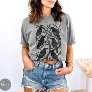 May include: Gray t-shirt featuring a black graphic of six crows perched on tree branches. The shirt is a relaxed fit and has short sleeves. The word "Gray" is printed on a gray circle in the lower left corner.