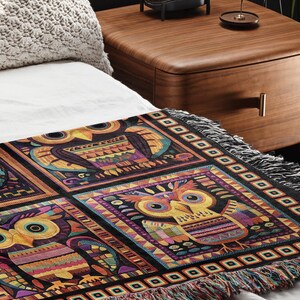 May include: A colorful throw blanket with a geometric pattern featuring owls. The blanket has a black background with colorful geometric shapes and owls in a repeating pattern. The blanket has fringe on all sides.