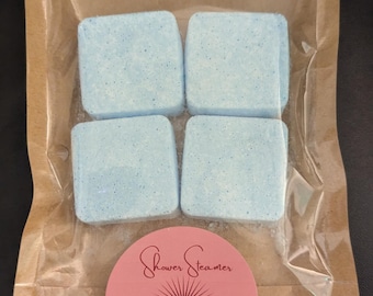 May include: A brown paper pouch with a clear plastic window, containing four blue shower steamers. The pouch has a pink circle sticker with the text "Shower Steamer" and "Aria Breathe".