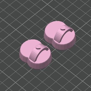 以下が含まれることがあります： 丸みを帯びたベースと湾曲した隆起部分を持つ、2つのピンク色の3Dレンダリングオブジェクト。それぞれ隆起部分に小さなハートのディテールがあります。オブジェクトは灰色のグリッドの背景に配置されています。