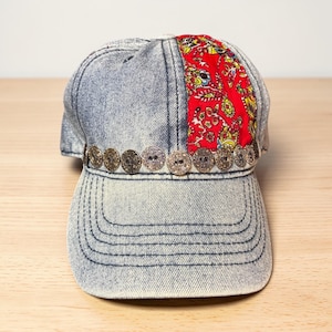 May include: A denim baseball cap with a red patterned fabric panel and decorative buttons. The cap features a curved brim and a series of small, round buttons along the front. The red fabric has a floral design.