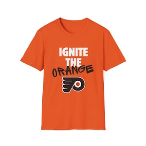 May include: Orange t-shirt with the text "IGNITE THE ORANGE" in white and black, along with a logo. The shirt is a solid orange color and has a crew neck.