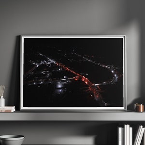 May include: A framed black and white photograph of a city at night with streetlights and a red bridge. The photograph is on a shelf with candles, a diffuser, and books.