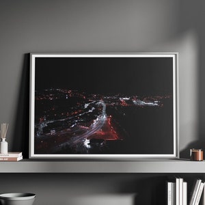 Puede incluir: Una fotografía enmarcada de una ciudad de noche, con un largo camino iluminado por farolas. La foto se muestra en un estante con velas, un difusor y libros.