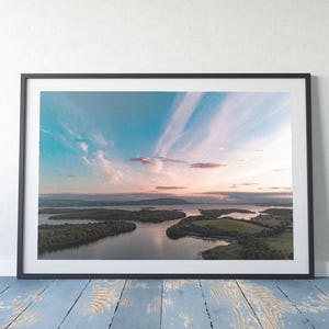 May include: An aerial view of a lake with several islands covered in green trees. The sky is a vibrant blue with streaks of pink and white clouds.