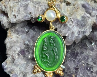 Puede incluir: Pendiente de oro con un camafeo verde que representa una figura religiosa, acentuado con piedras preciosas blancas y verdes.