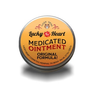 Może przedstawiać: Srebrny pojemnik z żółtą etykietą, na której widnieje napis "Lucky Heart Medicated Ointment Original Formula!" z logo głowy tygrysa i tekstem "Tiger Head est. 1935" nad nazwą produktu. Pojemnik ma 3,7 uncji lub 105 gramów.