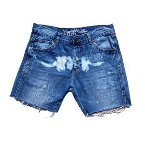 May include: Blue denim shorts with a distressed hem and a faded white design. The shorts have a Wrangler Retro Slim Straight label.