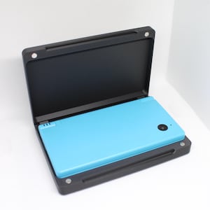 Op de afbeelding: Een zwarte draagtas met een blauw draagbaar spelapparaat erin. De tas is open en het apparaat is zichtbaar.