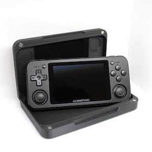 Op de afbeelding: Een zwarte handheld-gameconsole met een scherm, knoppen en joysticks. De console is open en zit in een zwarte draagtas.