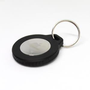 May include: A black keychain with a silver Apple logo in the center. The keychain has a silver ring attached to it.