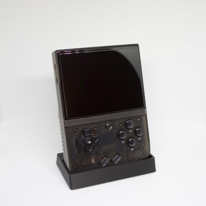 Op de afbeelding: Een zwarte handheld-gameconsole met een transparante behuizing. De console heeft een zwart-wit scherm, een directionele pad en knoppen met de labels 'A', 'B', 'Y', 'X', 'Start' en 'Select'.