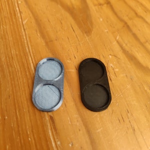 May include: Two round plastic trays, one is black and one is light blue. Each tray has two circular depressions.