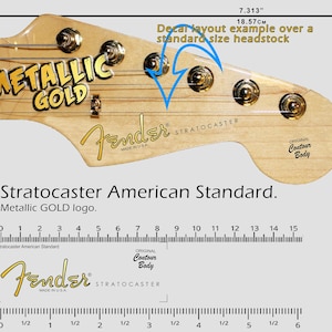 Puede incluir: Primer plano de una pala de guitarra con el logo "METALLIC GOLD" y la marca "Fender STRATOCASTER". La pala es de color marrón claro, con clavijas doradas y cuerdas. Medidas en cm, la pala mide 18,57 cm de largo.