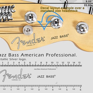 Może przedstawiać: Zbliżenie główki gitary basowej Fender Jazz z srebrnymi kluczami i napisem "METALLIC SILVER". Główka jest jasno brązowa. Obraz zawiera wymiary 23,00 cm i 9,05 cala. Widoczny jest również tekst "Jazz Bass American Professional".