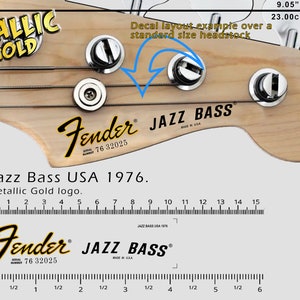 Könnte beinhalten: Nahaufnahme eines Fender Jazz Bass Kopfplatten-Decals. Das Decal ist metallisch goldfarben und enthält das Fender-Logo, den Jazz Bass-Text und die Seriennummer. Die Kopfplatte ist 23,00 cm breit, was 9,05 Zoll entspricht.