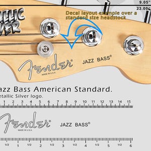 Może przedstawiać: Zbliżenie główki basu Fender Jazz z kluczami. Widoczne napisy "METALLIC SILVER" i "Jazz Bass American Standard". Szerokość główki to 23,00 cm, co odpowiada 9,05 cala.