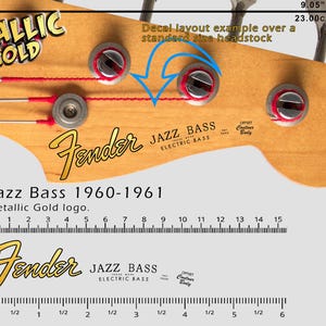 Könnte beinhalten: Nahaufnahme einer Fender Jazz Bass Kopfplatte mit metallisch goldenem Logo. Das Bild zeigt Maße in Zentimetern und Zoll sowie den Text "Jazz Bass 1960-1961".