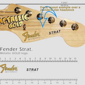 K&ouml;nnte beinhalten: Eine Gitarrenkopfplatte mit dem Fender Strat Logo in Metallic-Gold. Die Kopfplatte ist hellbraun mit goldenen Stimmwirbeln. Das Bild enth&auml;lt ein Lineal, das zeigt, dass die Kopfplatte 18,57 cm lang ist.