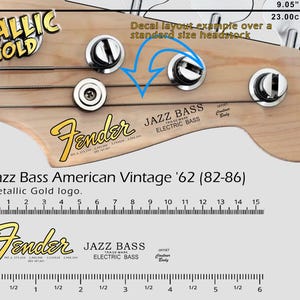 Può includere: Primo piano di una paletta di basso Fender Jazz con logo oro metallizzato. L'immagine include il testo "Jazz Bass American Vintage '62 (82-86)" e misure di 23,00 cm.