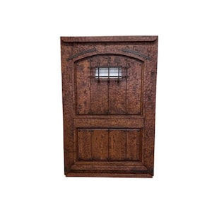 May include: A dark brown wooden door with a small, rectangular window with iron bars. The door has a raised, textured surface and a slightly arched top.