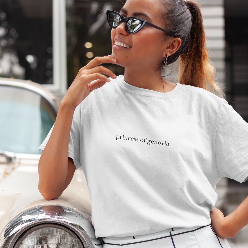 May include: White t-shirt with the text "princess of genovia" in a simple, black font. The shirt is being worn by a person wearing black sunglasses.