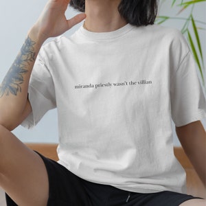 Pode incluir: Camiseta branca com o texto "miranda priestly wasn't the villian" impresso na frente.