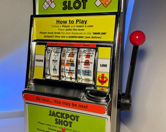 May include: A silver and green shot slot machine with a lever. The machine has a coin slot and a drink line. The machine has a variety of drink options, including rum, orange liqueur, and cranberry juice. The machine has a jackpot shot feature. The text on the machine reads "Shot Slot", "How to Play", "Drink Line", "Coin Slot", "Jackpot Shot", and "Please play responsibly".