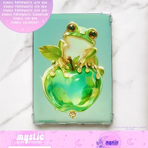 May include: A clear Kindle case featuring a vibrant illustration of a green frog perched on a green apple. The case has a light blue background. The text "Kindle Inserts" and "mysticbluustickers" are visible.