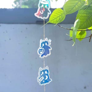 May include: A Halloween-themed hanging decoration with three cat-shaped figures in blue and iridescent colours. The top figure is a ghost cat, the middle one holds a pumpkin, and the bottom one has a crescent moon. A clear crystal ball hangs at the bottom.
