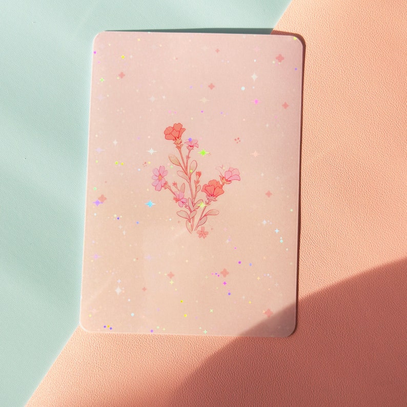 Puede incluir: Una tarjeta rosa con un dise&ntilde;o floral y un fondo brillante. Las flores son rosas y blancas y tienen un aspecto delicado y caprichoso.